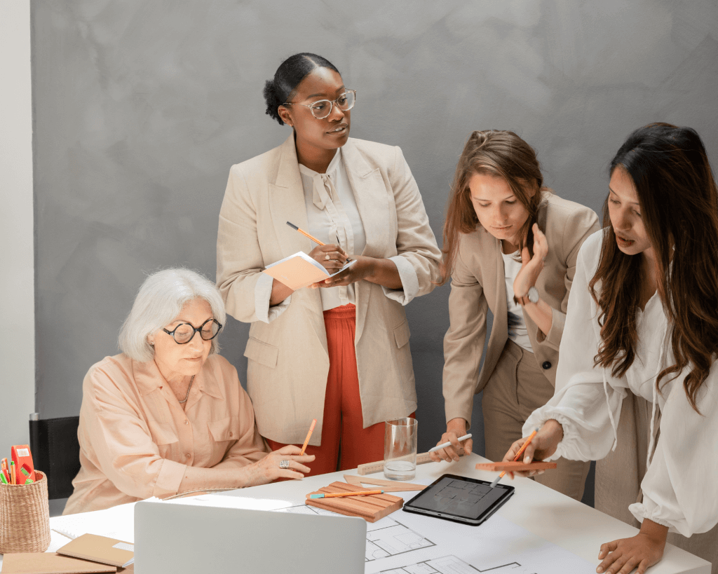 Scène intimiste montrant deux femmes professionnelles en discussion approfondie, avec carnets, ordinateur et livres de référence, dans un cadre feutré (bibliothèque ou bureau privé). 
